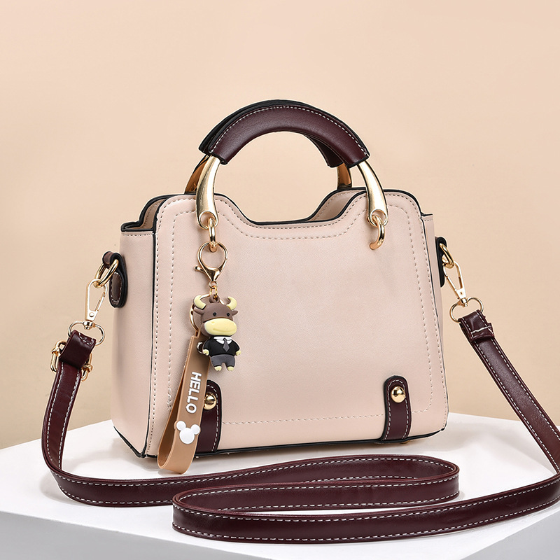 Trendy beige and maroon shell satchel bag with gold accents and keychain, featuring a zipper closure and dig bag design for easy access.